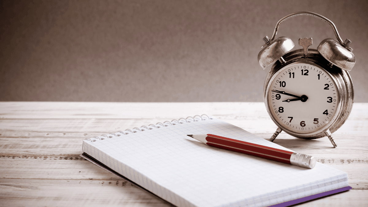 Um caderno com uma caneta e um despertador
